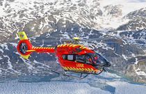 Rødt helikopter fra Norsk Luftambulanse som flyr over fjell